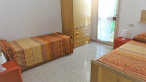 Camera da letto con due letti, un'armadio in legno, un comodino rosso e una finestra con vista sul verde.