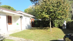 Una proprietà residenziale con vialetto in pietra, prato, un albero e una griglia per barbecue.