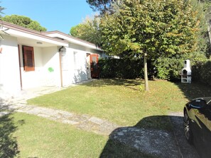 A residential property with a paved driveway, a lawn, a tree, and a barbecue grill. - Bibione Pineda Villa With Garden and BBQ (San Michele al Tagliamento)