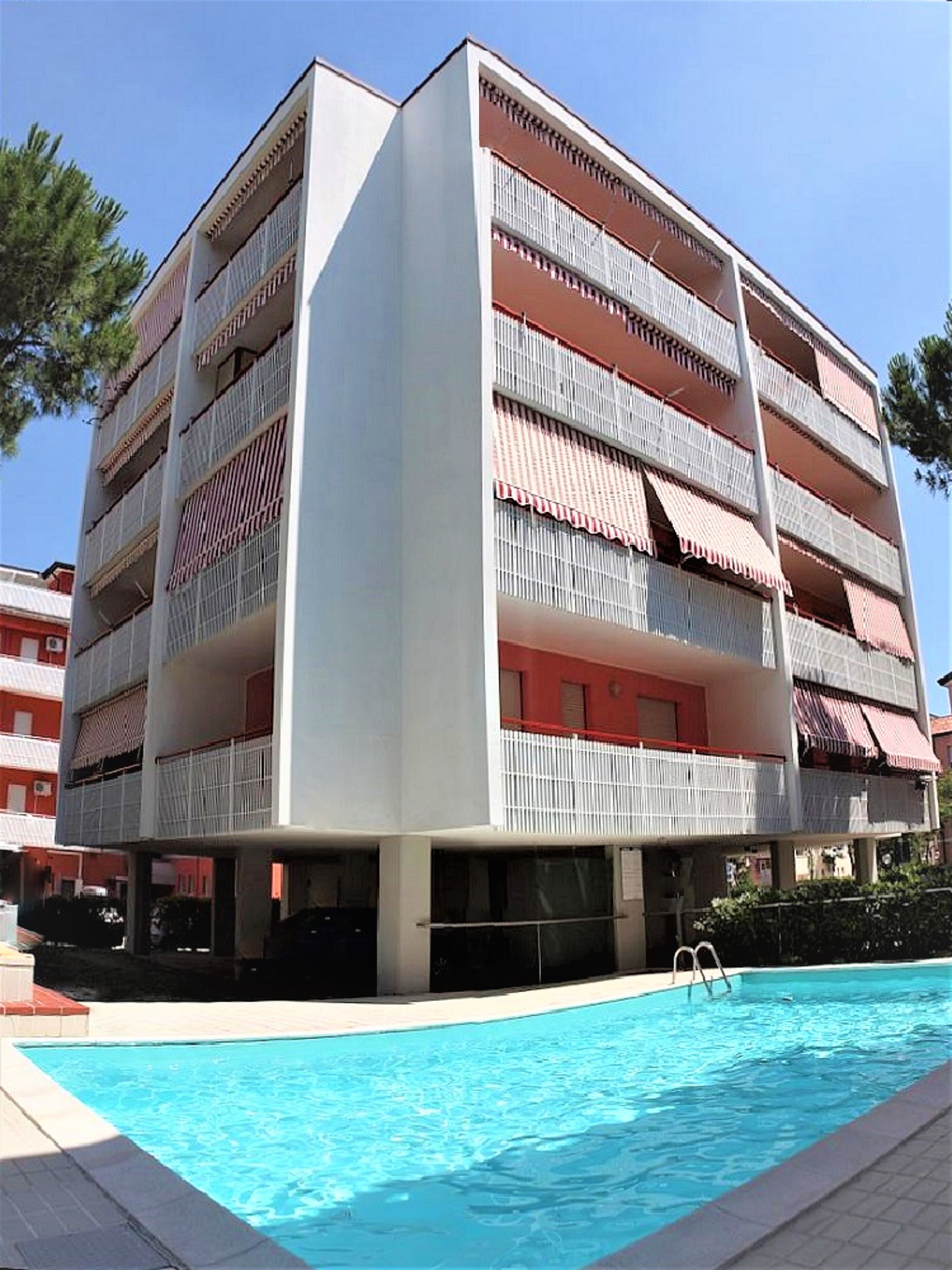 Un edificio de varios pisos con balcones, piscina y cielo despejado.