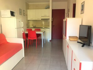 Un espacio habitable compacto con kitchenette, comedor y televisor sobre un mueble.