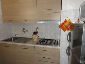 A kitchen with wooden cabinets, a gas stove, a sink, and a microwave. - Bibione Apartment With Side sea View (San Michele al Tagliamento)