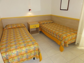 Una habitación pequeña y limpia, con dos camas individuales, una mesita de noche, una lámpara de pared y un espejo.