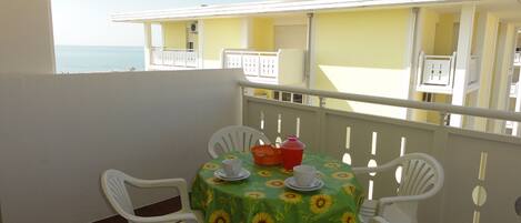 A balcony with a table set for two, white chairs, and a tablecloth with sunflowers.