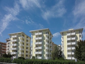 A row of three-story residential buildings with balconies, under a clear blue sky. - Bibione Apartment With Side sea View (San Michele al Tagliamento)