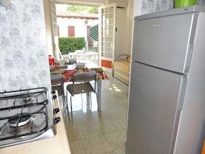 A kitchen with a gas stove, a refrigerator, and a dining table with chairs. - Quiet Apartment With Garden (San Michele al Tagliamento)