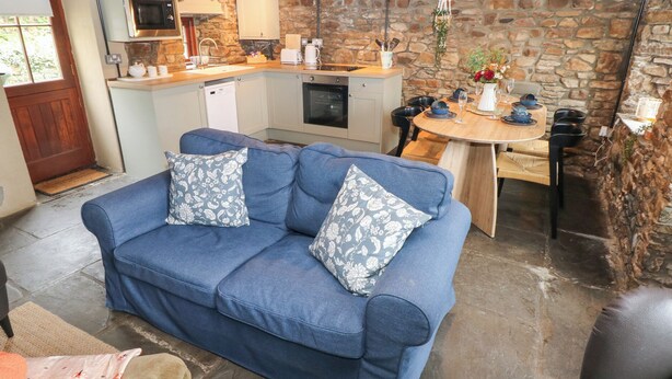 A cozy living area with a blue sofa and patterned cushions, a stone wall, and a kitchen with a stone countertop.