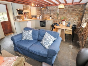 A cozy living area with a blue sofa and patterned cushions, a stone wall, and a kitchen with a stone countertop. - Melyn (Aberdare)