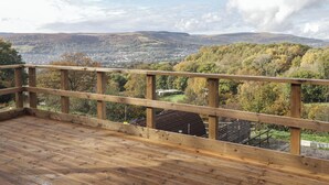 A wooden deck with a view of a town and hills in the distance.