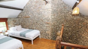 A bedroom with two beds, wooden flooring, stone walls, and a hanging light fixture.