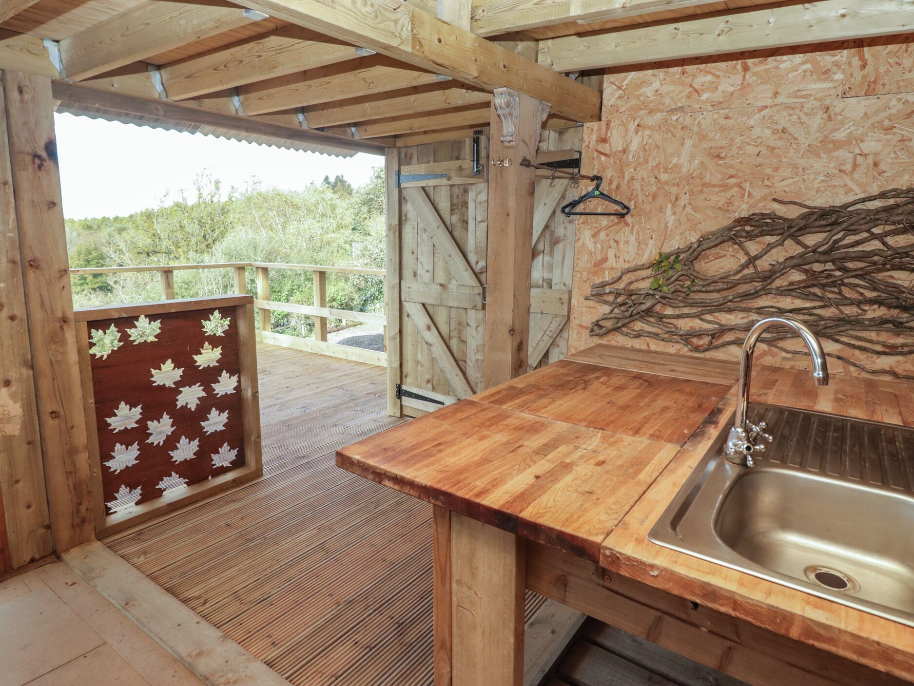 A wooden cabin with a wooden deck, a metal sink, and a view of trees.