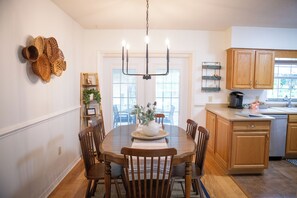 Un coin repas avec une table en bois, des chaises, un lustre et une vue sur la cuisine.