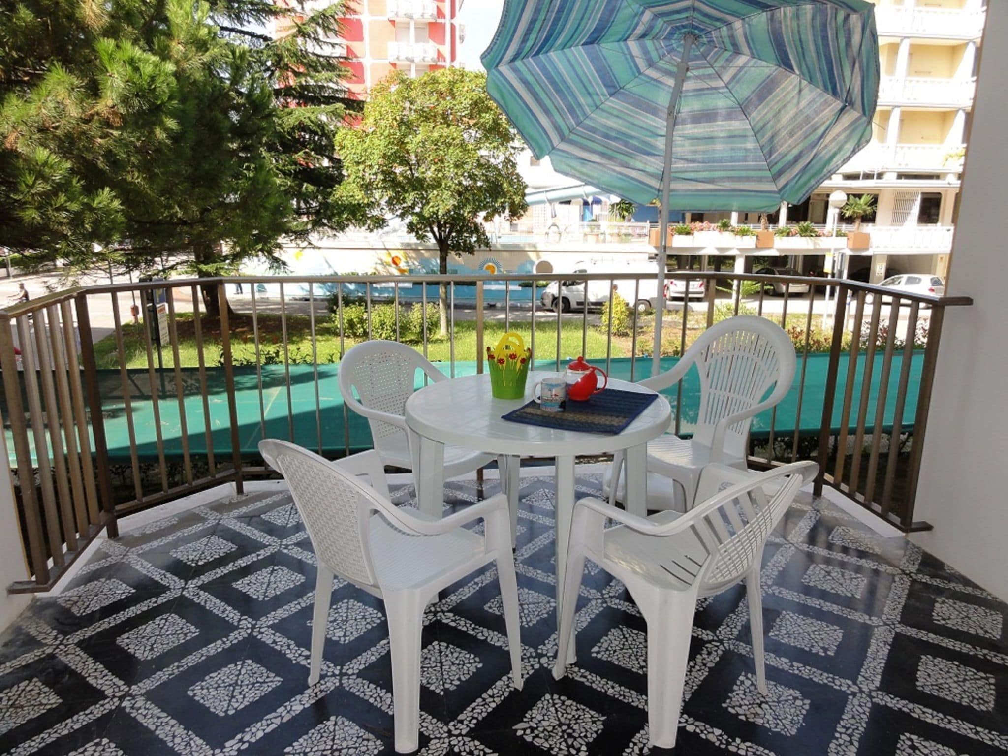 A balcony with a table and chairs, a patterned floor, and a view of a swimming pool and buildings.
