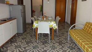 A compact kitchen with a refrigerator, a dining table with chairs, and a sofa. - Great Flat Close to the sea (San Michele al Tagliamento)
