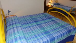 A room with two beds, each with a yellow metal frame and a blue and green plaid bedspread. There is a small table with a lamp between the beds. - Great Flat Close to the sea (San Michele al Tagliamento)