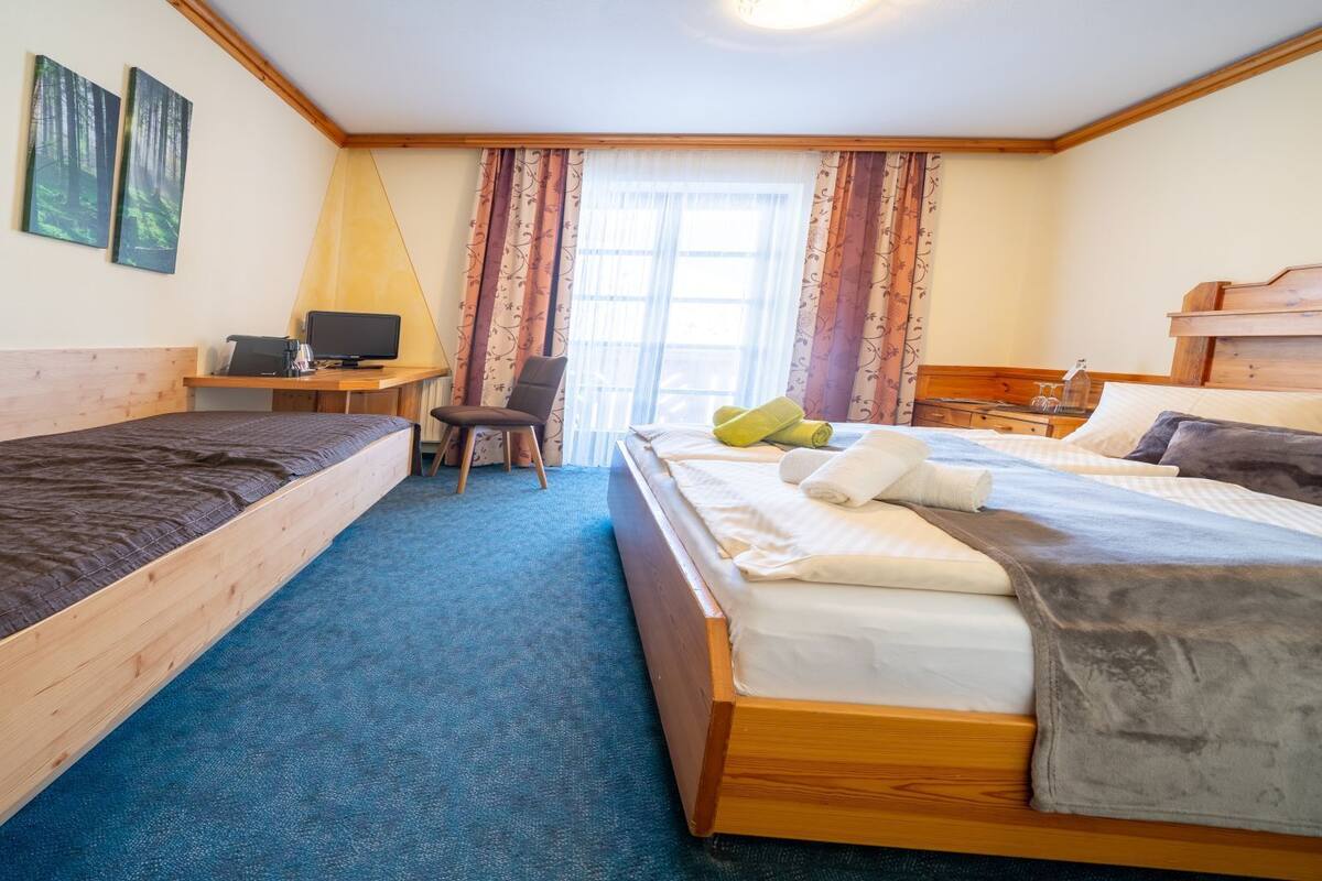 Ein Zimmer mit zwei Einzelbetten, einem Schreibtisch mit Computer, einem Stuhl und einem großen Fenster mit Vorhängen.