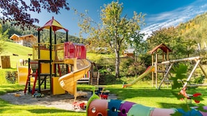 A playground with slides and climbing structures, surrounded by a grassy area and trees. - Familienhotel Unterreith (Forstau)