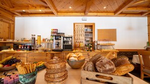 A kitchen area with wooden cabinets, a coffee machine, and various food items like bread and pastries. - Familienhotel Unterreith (Forstau)