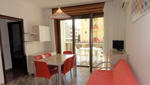 A room with a dining table, red chairs, a sofa, a TV, and a balcony with outdoor furniture. - Bright Flat Close to the sea (San Michele al Tagliamento)