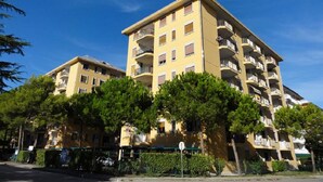 A multi-story residential building with balconies, surrounded by trees and a clear sky. - Bright Flat Close to the sea (San Michele al Tagliamento)