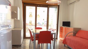 A compact room with a dining table, chairs, a sofa, a TV, and a kitchenette. - Bright Flat Close to the sea (San Michele al Tagliamento)
