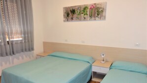 A hotel room with two beds, a nightstand, a lamp, and a floral artwork on the wall. - Bright Flat Close to the sea (San Michele al Tagliamento)