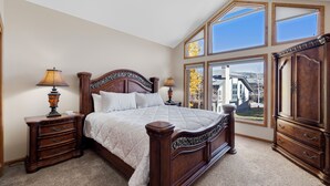 Une chambre à coucher avec un grand lit, deux tables de chevet, une armoire et une fenêtre donnant sur un immeuble.