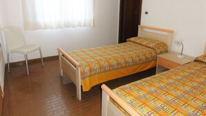 A bedroom with a bed, a chair, a nightstand, and a window with curtains. - Semi-detached Villa in a Quiet Area (San Michele al Tagliamento)
