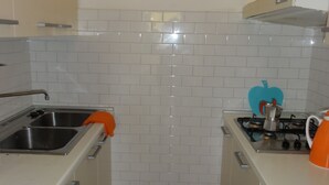 A compact kitchen with white cabinets, a stainless steel sink, a gas stove, and a blue apple-shaped soap dispenser. - Semi-detached Villa in a Quiet Area (San Michele al Tagliamento)