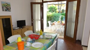 A dining area with a table set for four, a television on a cabinet, and a view of an outdoor patio with a table and chairs. - Semi-detached Villa in a Quiet Area (San Michele al Tagliamento)