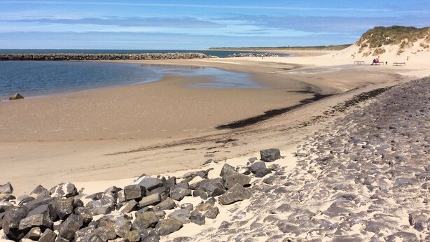 En strand med en klippefyldt kystlinje, et roligt hav og en klar himmel.