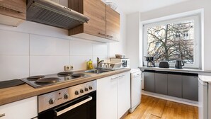 Een moderne keuken met een kookplaat, oven en vaatwasser, houten kastjes en een raam met uitzicht op gebouwen.