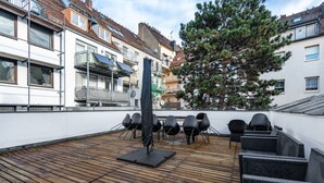 Een terras op het dak met houten vloer, buitenmeubels en uitzicht op woongebouwen.