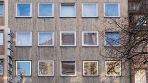 Een meerlaags gebouw met een gelijkmatige gevel, meerdere ramen en een zichtbaar bord aan de linkerkant.