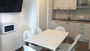 A compact kitchen with white cabinets, a microwave, a stove, and a TV mounted above the counter. - Modern Terraced House (San Michele al Tagliamento)