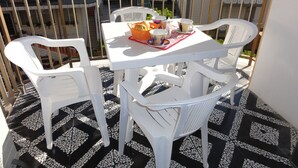 A balcony with a white table and chairs, a tray with cups and a basket of bread, and a patterned floor. - Nice Flat Close to the sea (San Michele al Tagliamento)