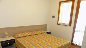A bedroom with a bed, a nightstand, a lamp, and a window with curtains. - Comfy Terraced House (San Michele al Tagliamento)