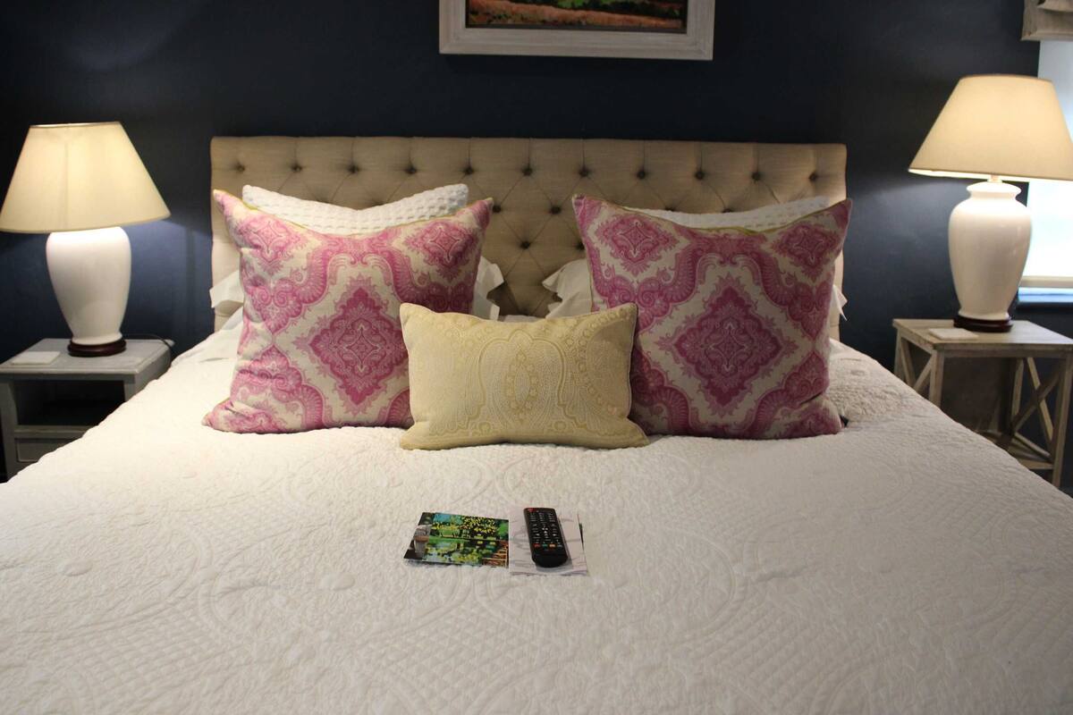 A bed with a tufted headboard, two bedside lamps, and three patterned pillows.