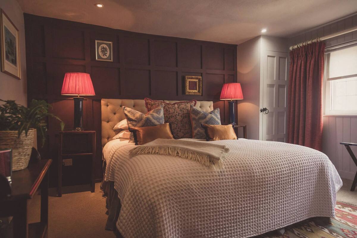 A bedroom with a large bed, two bedside lamps, a tufted headboard, and a framed picture on the wall.