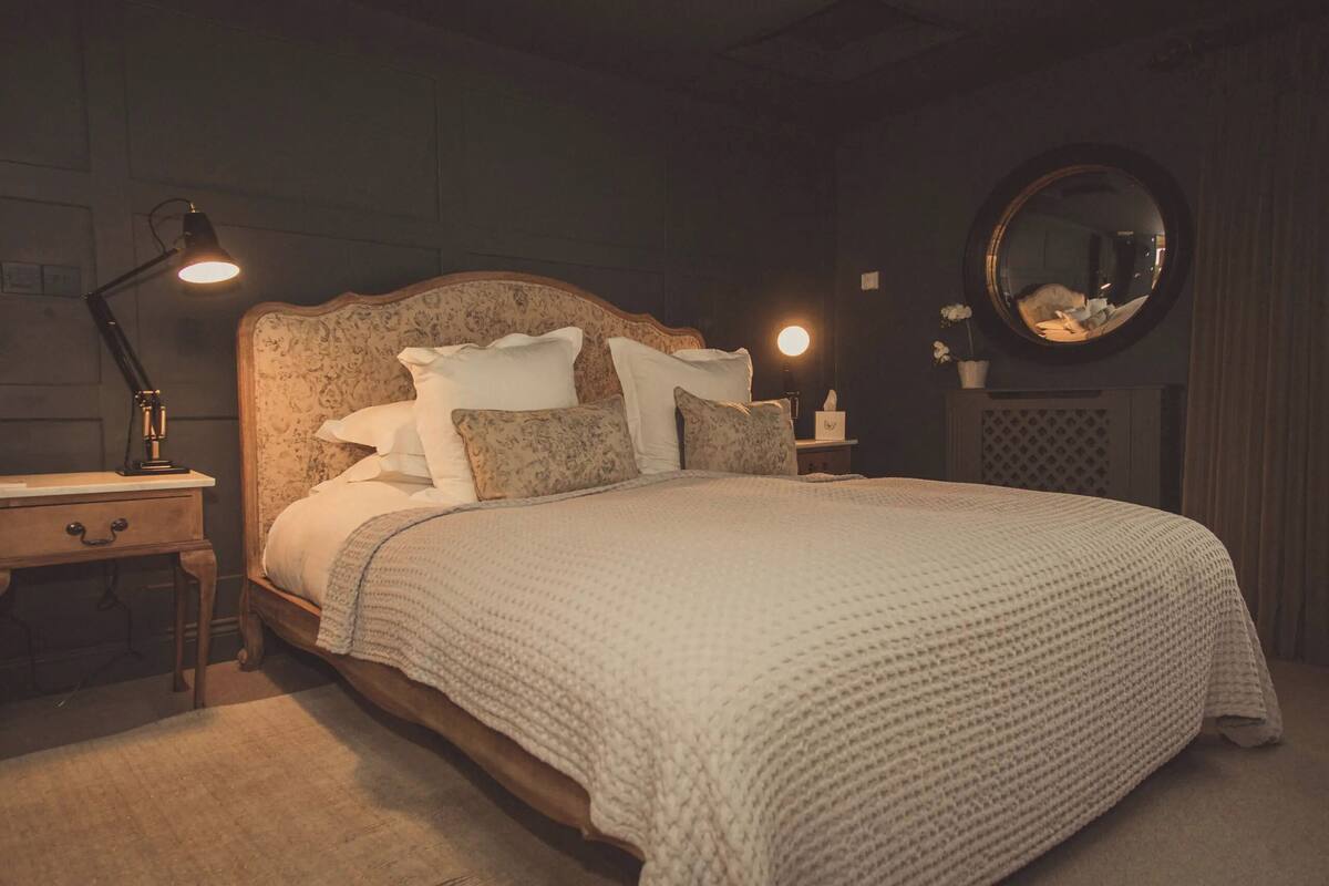 A bedroom with a large bed, a nightstand, a lamp, a mirror, and a dresser.