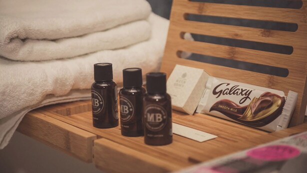 A wooden bench with a Galaxy chocolate bar, three bottles of liquid, and folded towels. - The Greyhound on the Test (Stockbridge)