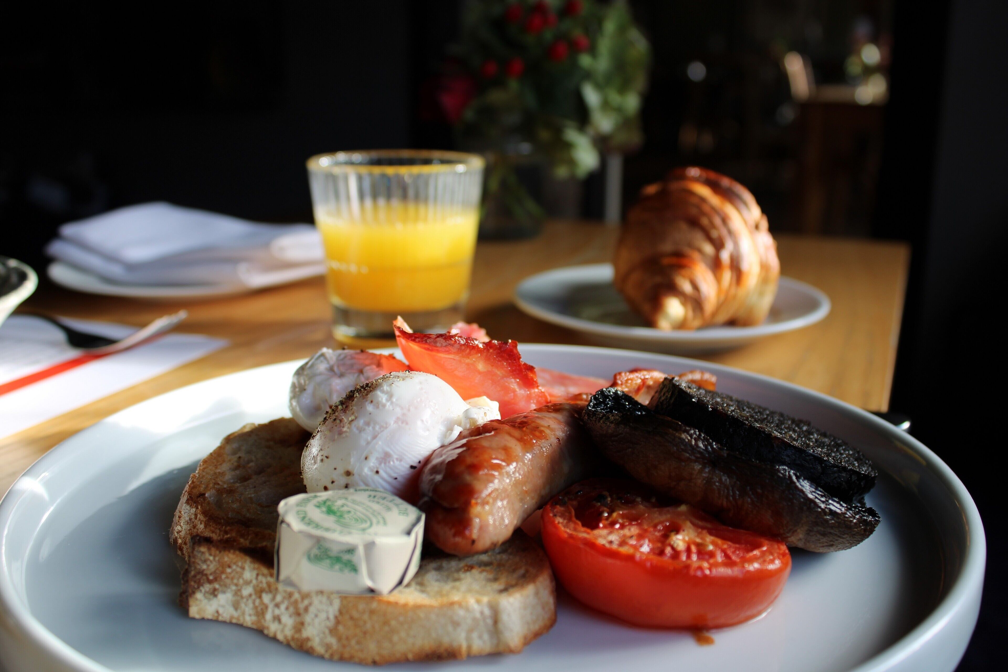 Une assiette de petit-déjeuner avec des toasts, des saucisses, des tomates et un croissant.