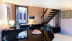 A modern dining area with a round table, black chairs, and a plate of fruit. A staircase with a black railing is visible in the background. - Rental in Rome Navona Loft (Rome)