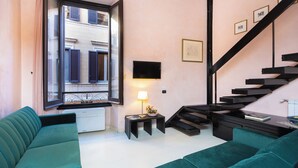 A modern living room with a sofa, a small table with a lamp, and a staircase. - Rental in Rome Navona Loft (Rome)