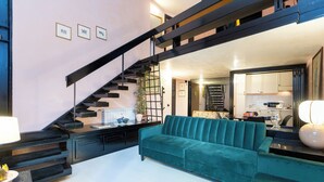 A modern living room with a teal sofa, a staircase, and a kitchen area visible through an open door. - Rental in Rome Navona Loft (Rome)