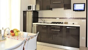 A modern kitchen with dark cabinets, a stainless steel refrigerator, a microwave, and a gas stove.