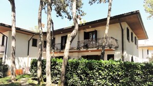 A two-story building with a balcony, surrounded by trees and a well-maintained hedge. - Terraced House With Garden (San Michele al Tagliamento)