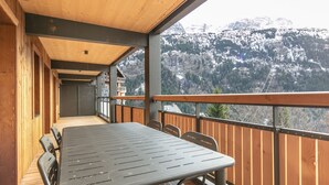 A wooden deck with a table and chairs, overlooking a mountainous landscape.