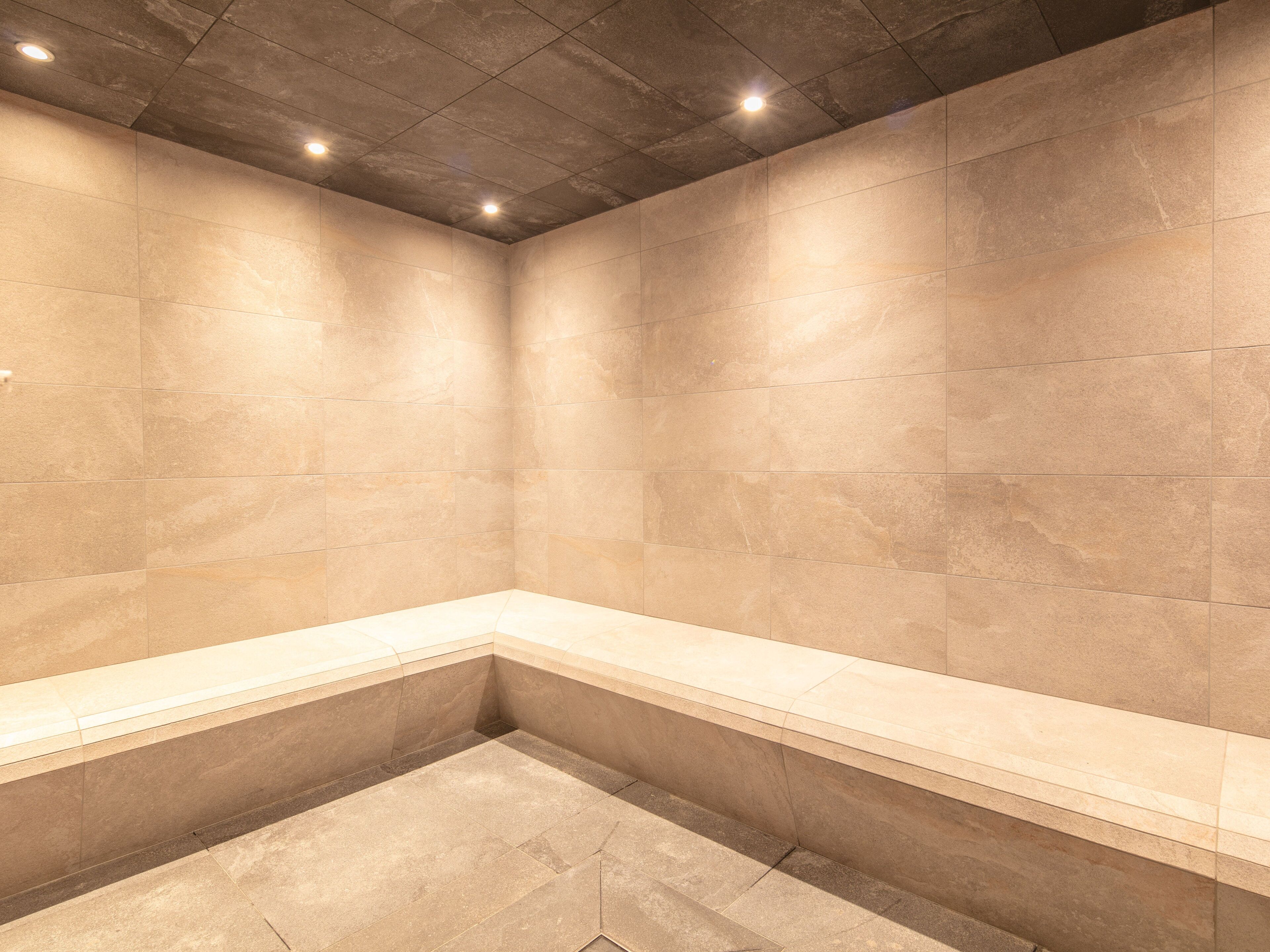 A modern bathroom with beige tiles, a bench, and recessed lighting.