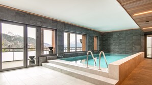 Una piscina interior con vistas a montañas, paredes de piedra y techo de madera.